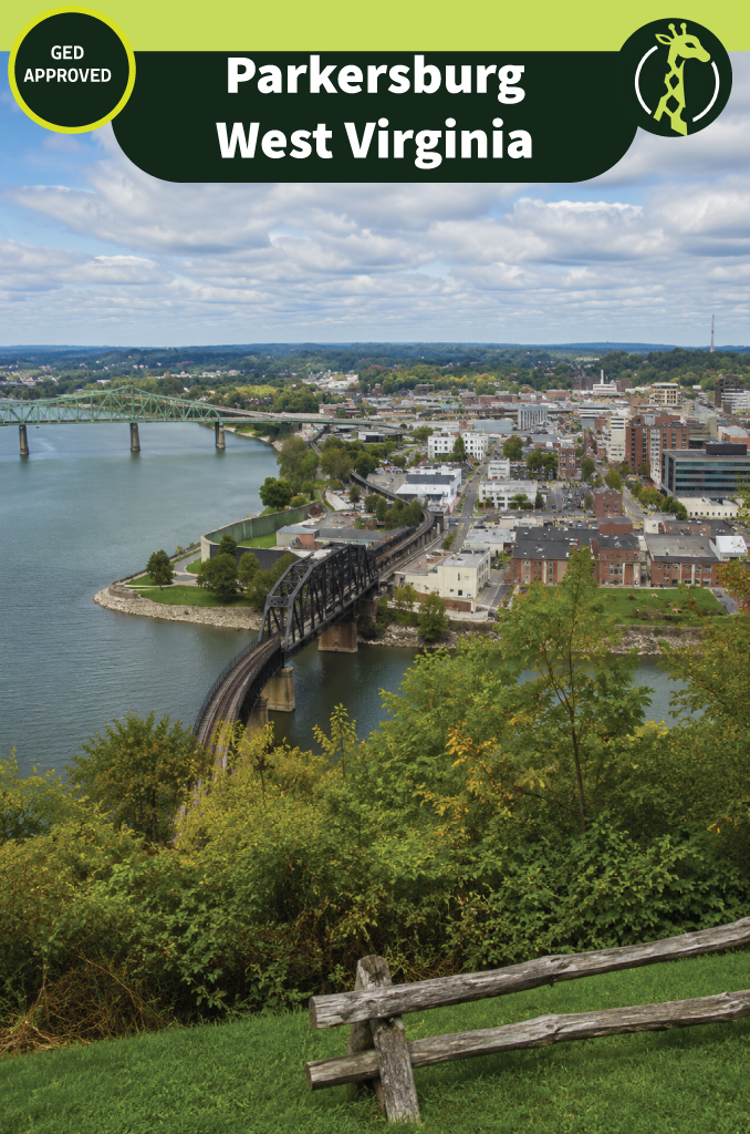 Parkersburg, West Virginia seen from a wooded hillside, with a green truss bridge and a black railroad bridge crossing the Ohio River toward the downtown blocks.